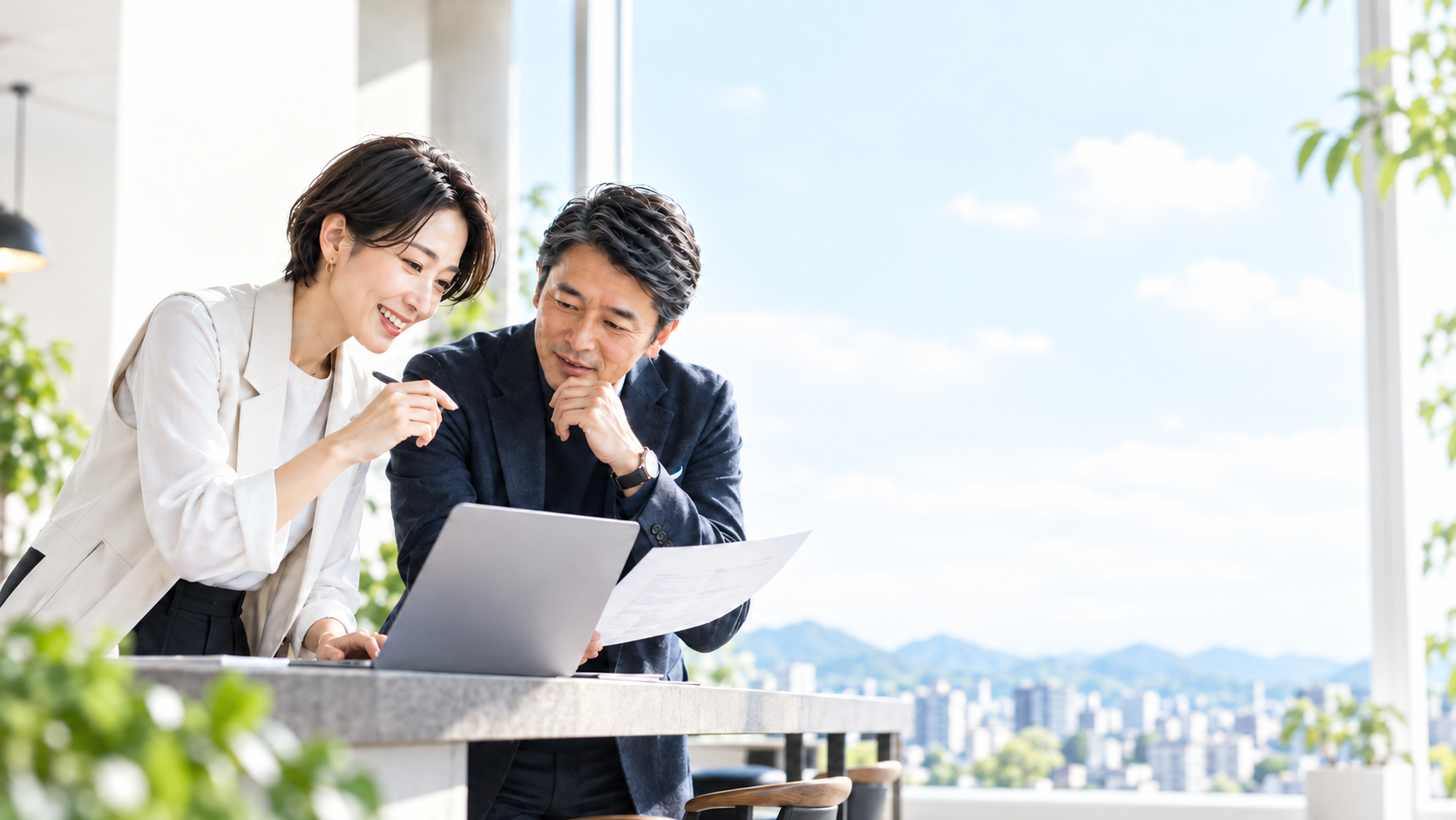 パソコンと資料を見ながら業務改善について話し合う二人